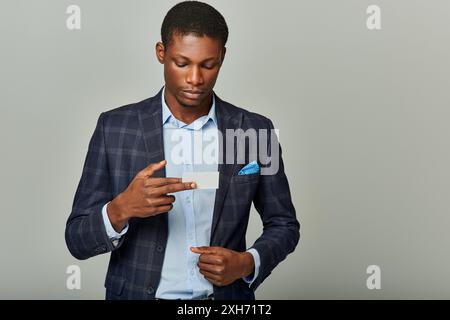 Afroamerikanischer Geschäftsmann in schicker Suite mit Visitenkarte vor grauem Hintergrund. Stockfoto