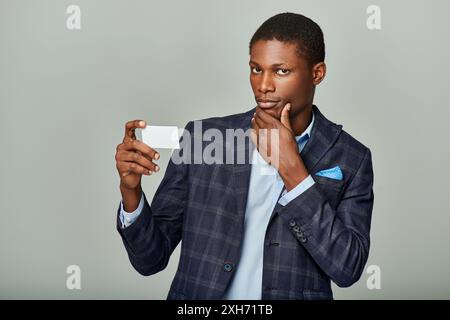 Afroamerikanischer Geschäftsmann in kariertem Blazer mit Visitenkarte auf grauem Hintergrund. Stockfoto