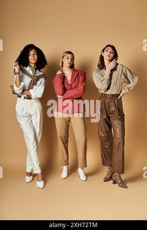 Drei junge, schöne multikulturelle Frauen in stilvoller Kleidung, die nebeneinander auf beigefarbenem Hintergrund stehen. Stockfoto