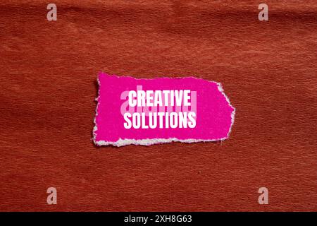 Creative Solutions Message geschrieben auf gerissenem rosafarbenem Papierstück mit braunem Hintergrund. Symbol für konzeptionelle kreative Lösungen. Kopierbereich. Stockfoto