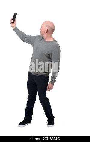 Ansicht eines drehenden Mannes, der ein Selbstporträt mit Smartphone auf weißem Hintergrund macht Stockfoto