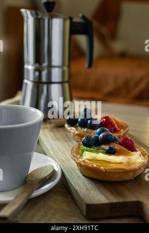 Nahaufnahme eines Kuchens mit Obst, einer Tasse Kaffee und einer Kaffeekanne im Hintergrund. Snack im Wohnzimmer Stockfoto