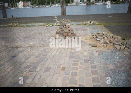 Flensburg, Schleswig-Holstein Dampfrundum 2024 Flensburg, die Veranstaltung wird 2024 aufgrund der Schäden durch das Ostseesturmhochwasser im Oktober 2023 an einem zwei Orten stattfinden. Die Organisatoren müssen auf den angestammten Platz an der südlichen Schiffbrücke verzichten, da die Kaikante dort abgesackt ist. Eine Absperrung wurde errichtet, hier: Blick von der Westseite des Flensburger Hafens zur Ostseite über das Hafenbecken. Weiter im Bild Asphalt-Steine werden zu kunstvoll anmutenden Aufbauten gestapelt. Aufnahme vom 12.07.2024, Flensburg, Hafen West *** Flensburg, Schleswig Holstei Stockfoto
