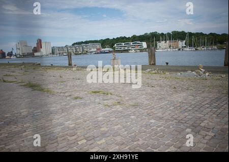Flensburg, Schleswig-Holstein Dampfrundum 2024 Flensburg, die Veranstaltung wird 2024 aufgrund der Schäden durch das Ostseesturmhochwasser im Oktober 2023 an einem zwei Orten stattfinden. Die Organisatoren müssen auf den angestammten Platz an der südlichen Schiffbrücke verzichten, da die Kaikante dort abgesackt ist. Eine Absperrung wurde errichtet, hier: Blick von der Westseite des Flensburger Hafens zur Ostseite über das Hafenbecken. Weiter im Bild Asphalt-Steine werden zu kunstvoll anmutenden Aufbauten gestapelt. Aufnahme vom 12.07.2024, Flensburg, Hafen West *** Flensburg, Schleswig Holstei Stockfoto