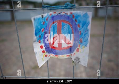 Flensburg, Schleswig-Holstein Dampfrundum 2024 Flensburg, transparent mit Zeichen Frieden am Bauzaun. Die Veranstaltung wird 2024 aufgrund der Schäden durch das Ostseesturmhochwasser im Oktober 2023 an einem zwei Orten stattfinden. Die Organisatoren müssen auf den angestammten Platz an der südlichen Schiffbrücke verzichten, da die Kaikante dort abgesackt ist. Eine Absperrung wurde errichtet, hier: Blick von der Westseite des Flensburger Hafens zur Ostseite über das Hafenbecken. Weiter im Bild Asphalt-Steine werden zu kunstvoll anmutenden Aufbauten gestapelt. Aufnahme vom 12.07.2024, Flensburg, Stockfoto