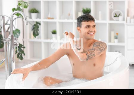 Hübscher junger Mann, der sich zu Hause in der Badewanne den Rücken massiert Stockfoto