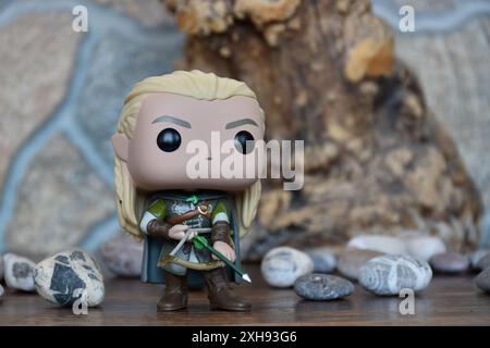 Funko Pop Vinyl Actionfigur von Elf Legolas aus dem Fantasy-Film der Herr der Ringe. Krieger in Rüstung, der Bogen und Pfeil hält. Alter Baum, Steine. Stockfoto