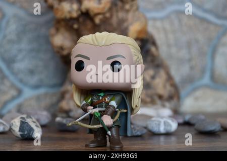 Funko Pop Vinyl Actionfigur von Elf Legolas aus dem Fantasy-Film der Herr der Ringe. Krieger in Rüstung, der Bogen und Pfeil hält. Alter Baum, Steine. Stockfoto