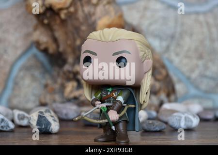 Funko Pop Vinyl Actionfigur von Elf Legolas aus dem Fantasy-Film der Herr der Ringe. Krieger in Rüstung, der Bogen und Pfeil hält. Alter Baum, Steine. Stockfoto