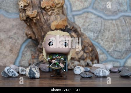 Funko Pop Vinyl Actionfigur von Elf Legolas aus dem Fantasy-Film der Herr der Ringe. Krieger in Rüstung, der Bogen und Pfeil hält. Alter Baum, Steine. Stockfoto