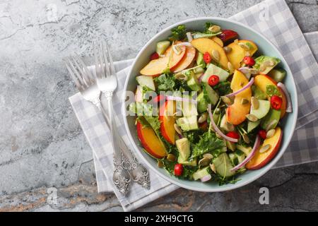 Frischer Sommersalat mit Pfirsich, Avocado, Gurke, roten Zwiebeln, Chili, Rucola, Spinat und Kürbiskerne aus nächster Nähe in einer Schüssel auf dem Tisch. Horizontal oben Stockfoto