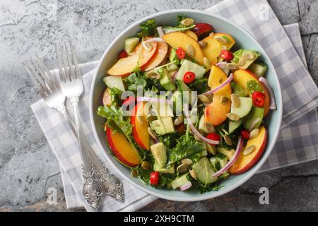 Würziger Salat mit Nektarine, Avocado, Gurke, roten Zwiebeln, Chili, Rucola, Spinat und Kürbiskerne aus nächster Nähe in einer Schüssel auf dem Tisch. Horizontal oben VI Stockfoto