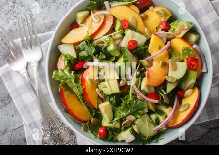 Veganer Vitaminsalat mit Pfirsich, Avocado, Gurke, roten Zwiebeln, Chili, Rucola, Spinat und Kürbiskerne aus nächster Nähe in einer Schüssel auf dem Tisch. Horizontal bis Stockfoto