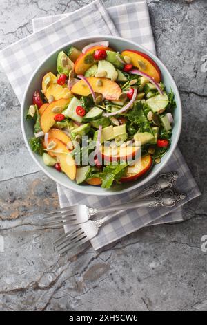 Vegetarischer Peach Avocado Salat mit roten Zwiebeln, Chili, Rucola, Spinat und Kürbiskernen in einer Schüssel auf dem Tisch. Verti Stockfoto