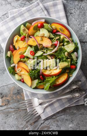 Hausgemachter Salat mit Nektarine, Avocado, Gurke, roten Zwiebeln, Chili, Rucola, Spinat und Kürbiskerne aus nächster Nähe in einer Schüssel auf dem Tisch. Vertikal oben V Stockfoto