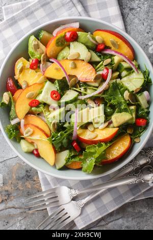 Pfirsichavocadosalat mit Zwiebeln, Chili, Rucola, Spinat und Kürbiskernen in einer Schüssel auf dem Tisch. Vertikale Draufsicht von oben Stockfoto