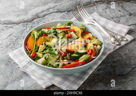 Veganer Vitaminsalat mit Pfirsich, Avocado, Gurke, roten Zwiebeln, Chili, Rucola, Spinat und Kürbiskerne aus nächster Nähe in einer Schüssel auf dem Tisch. Horizontal Stockfoto