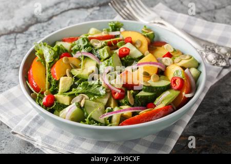 Würziger Salat mit Nektarine, Avocado, Gurke, roten Zwiebeln, Chili, Rucola, Spinat und Kürbiskerne aus nächster Nähe in einer Schüssel auf dem Tisch. Horizontal Stockfoto