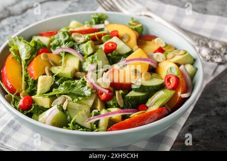 Frischer Sommersalat mit Pfirsich, Avocado, Gurke, roten Zwiebeln, Chili, Rucola, Spinat und Kürbiskerne aus nächster Nähe in einer Schüssel auf dem Tisch. Horizontal Stockfoto