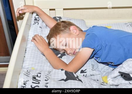 Das Bild zeigt einen schlafenden Jungen, der auf dem Bett auf dem Bauch schläft. Stockfoto