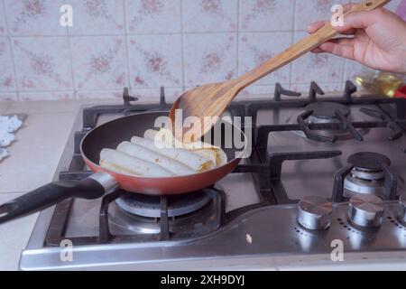 Zubereitung goldener Tacos in der Pfanne, Braten mexikanischer Tacos, in einer mexikanischen Küche im Vordergrund. Stockfoto