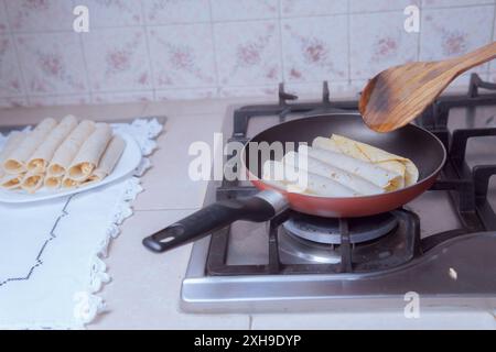 Zubereitung goldener Tacos in der Pfanne, Braten mexikanischer Tacos, in einer mexikanischen Küche im Vordergrund. Stockfoto