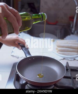 Wenn man Öl in die heiße Pfanne gießt, in einer mexikanischen Küche, werden nur weibliche Hände gesehen, die den Ölkolben halten. Stockfoto