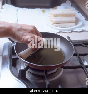 Zubereitung von frittierten Tacos in einer Pfanne, Sie können nur einige Hände sehen, die einige Tacos in die Pfanne geben, traditionelle mexikanische Küche. Stockfoto