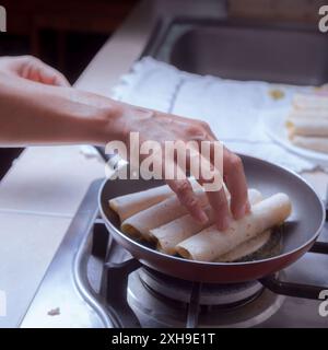 Zubereitung von frittierten Tacos in einer Pfanne, Sie können nur einige Hände sehen, die einige Tacos in die Pfanne geben, traditionelle mexikanische Küche. Stockfoto