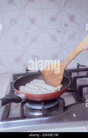 Zubereitung goldener Tacos in der Pfanne, Braten mexikanischer Tacos, in einer mexikanischen Küche im Vordergrund. Stockfoto