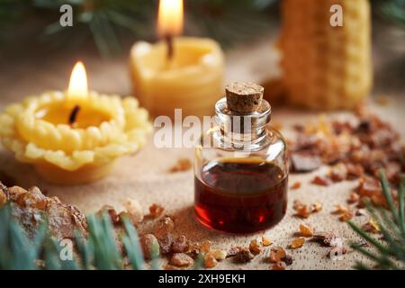 Eine Flasche ätherisches Myrrhenöl und Harz mit Kerzen aus Bienenwachs im Hintergrund. Aromatherapie oder Alternativmedizin. Stockfoto