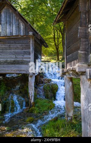 Ein kleiner Bach mit kristallklarem Wasser fließt über einen steilen Hang zwischen zwei Hütten. Stockfoto