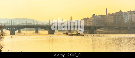 Die Jirasek-Brücke in Prag, Tschechien, überspannt die Moldau bei Sonnenuntergang. Die Brücke ist ein beliebter Ort für Spaziergänge und die Skyline der Stadt zu bewundern. Das goldene Licht der untergehenden Sonne wirft ein warmes Licht über die Stadtlandschaft. Stockfoto