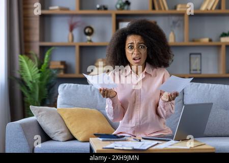 Besorgte Frau, die Papiere hält, die Ausgaben mit Laptop zu Hause berechnen. Finanzieller Stress und Budgetkonzept. Stockfoto