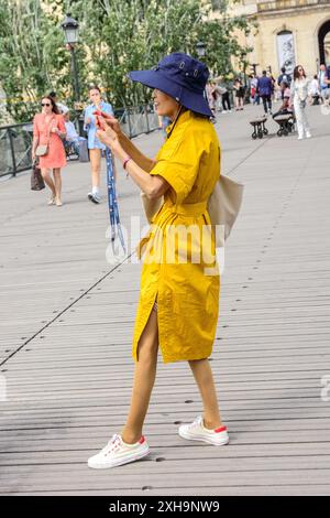 Orientalische Touristin in elegantem gelbem Kleid auf der Fußgängerbrücke Pont du Carrousel und macht ein Telefonfoto - Paris 75001, Frankreich. Stockfoto