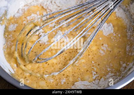 Schüssel mit Teig und Schneebesen auf Holztisch. Nahaufnahme des Mischteigs für Bäckerei und Kochen. Zutaten für Waffeln, Kuchen oder Pfannkuchen. Teig Stockfoto