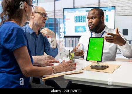 Senioren erkunden mit Berater Optionen für die Altersvorsorge und diskutieren neben der Chroma-Schlüsselanzeige auf dem Tablet. Sicherung des Schutzes von Lebensersparnissen und des Wachstums für die Zukunft. Stockfoto