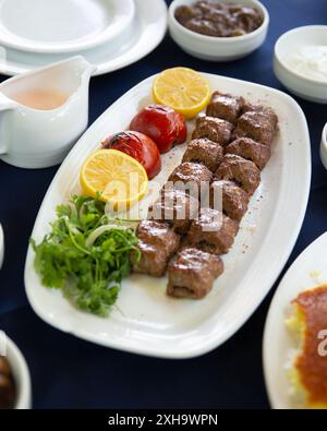 Teller persischer Kebabs serviert mit gegrillten Tomaten, frischen Kräutern und Zitrone, ein klassisches Gericht aus dem Nahen Osten. Stockfoto