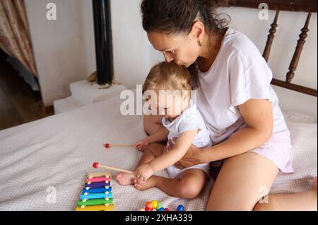 Eine Mutter genießt spielerische Momente mit ihrem Baby auf dem Bett und konzentriert sich dabei auf Familienbindung und frühkindliche Entwicklung. Das Bild fängt Liebe, Sorgfalt, an ein Stockfoto