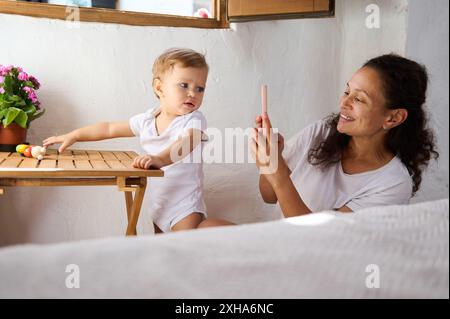 Mutter macht ein Foto von ihrem neugierigen Kleinkind drinnen. Die Szene fängt einen herzlichen Familienmoment ein, bei dem das Kind die Erkundung und die Mutter die schätzen Stockfoto