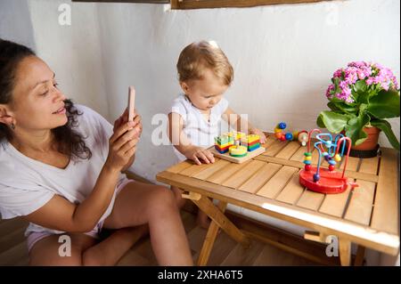 Eine Mutter fängt einen Moment ein, in dem ihr Kind zu Hause mit pädagogischem Spielzeug spielt. Die Szene ist warm, intim und voller freudiger Lernfreude. Stockfoto