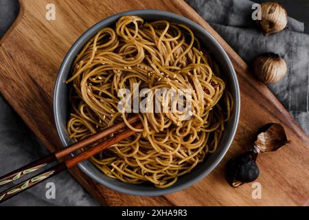 Black Knolic Sesam Noodles serviert in einer Schüssel mit Stäbchen: Aus nächster Nähe von Stäbchen, die in Nudeln und gerösteter Knoblauch-Sesam-Sauce gewickelt sind Stockfoto