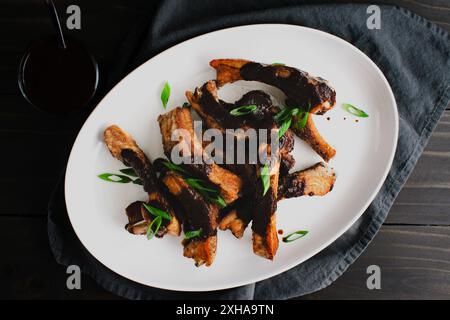 Schweinerippchen mit schwarzer Knoblauch-Miso-Sauce auf einem Servierteller: Platte mit Baby-Back-Rippchen in herzhafter Barbecue-Sauce garniert mit Zwiebeln Stockfoto