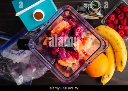 Zutaten in einem Mixer für Raspberry Orange Smoothie Bowl: Unvermischte gefrorene Himbeeren, Orange und Banane mit Mandelmilch und Ahornsirup Stockfoto