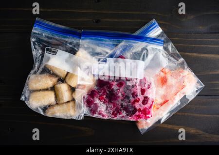 Beutel mit portioniertem gefrorenem Obst mit leeren Etiketten: Gefrorene Bananen, Himbeeren und cara cara Orange auf einem Holztisch Stockfoto