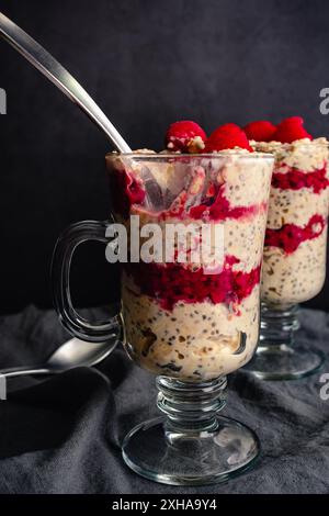 Himbeere Erdnussbutter Haferparfaits mit Löffel: Gesundes mehrschichtiges Frühstück mit Himbeeren, gerollten Ocken, Obst und Chiasamen in irischen Kaffeegläsern Stockfoto
