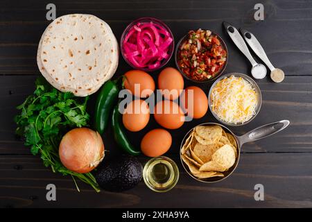 Tex-Mex Migas Frühstück Tacos Zutaten: Eier, Tortilla Chips, Jalapeno Paprika, Mehltortillas, geriebener Käse, und mehr auf einem Holztisch Stockfoto