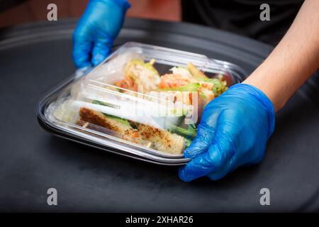 Eine Ansicht eines Mitarbeiters, der sich darauf vorbereitet, in einem Restaurant in einer Küche Lebensmittel zum Mitnehmen zu verpacken. Stockfoto