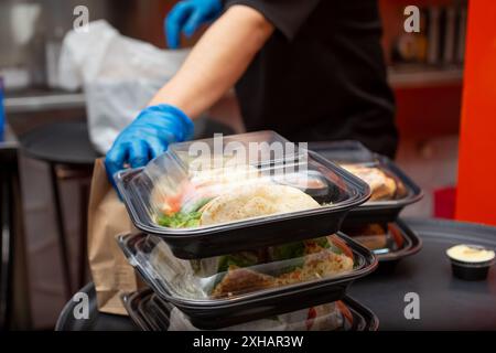 Ein Blick auf einen Mitarbeiter, der sich darauf vorbereitet, mehrere Lebensmittelbehälter für unterwegs in einer Restaurantküche zu verpacken. Stockfoto