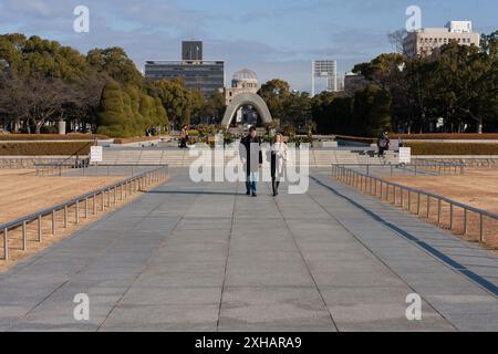 Hiroshima, Japan. Januar 2010. Westliche Touristen laufen in Richtung Atombombenmuseum in Hiroshima mit einer Bombenkuppel und einem Bogen des Memorial Cenotaph dahinter. Ursprünglich die Hiroshima Prefectural Commercial Hall, wurde die Atombombenkuppel, wie sie heute bekannt ist, zu einem Wahrzeichen, da sie eines der wenigen Bauwerke war, die nach dem Atombombenanschlag auf Hiroshima am 6. August 1945 noch stehen geblieben waren. Im Dezember 1996 zum UNESCO-Weltkulturerbe erklärt. (Foto: Damon Coulter/SOPA Images/SIPA USA) Credit: SIPA USA/Alamy Live News Stockfoto